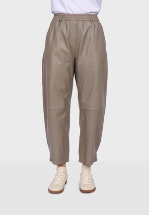 Taupe high-waist faux leather pants with elastic waistband and tapered legs worn with off-white sneakers and white socks on a light background.