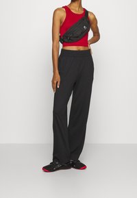 Červený krátký top bez rukávů s kulatým výstřihem, černé kalhoty s vysokým pasem a černé boty s červenými detaily. Doplněno černou taškou přes rameno.