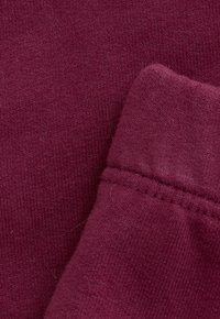 Detailopname van zachte, ribbelige bordeauxrode stof met zichtbare stiksels en gevouwen naaddetail.