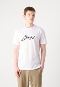 Fehér pamut póló, amelyen elöl egy fekete, írott "Boss" logó található. Rövid ujjú és kerek nyakú kialakítás. Simább szövet.