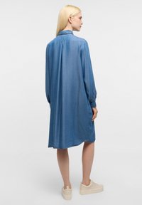 Abito camicia in denim azzurro chiaro, con maniche lunghe, vestibilità rilassata e orlo curvo. Indossato con sneakers piattaforme beige.