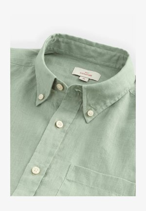 Cămașă din in verde deschis, cu butoni, guler, buzunar frontal și butoane albe. Etichetele includ "NEXT" și "SIGNATURE," mărimea Medie.