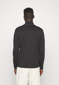 Camicia nera a maniche lunghe con colletto alto, realizzata in tessuto morbido. Presenta un corpetto aderente con maniche leggermente affusolate e un orlo curvo.