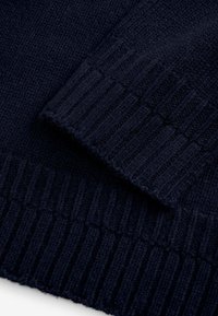 Pulover tricotat de culoare albastru marin, cu mansete și tiv cu nervuri. Textură moale, cusături detaliate și un finisaj neted pun în evidență designul său.