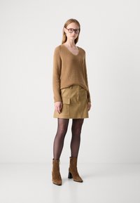 Brun strikket genser med V-hals, parret med en beige cargoskjørt med frontlommer. Modellen har på seg svarte strømpebukser og brune ankelstøvler.