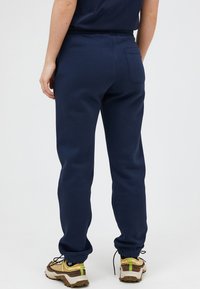 Marineblå sweatpants med elastisk talje og manchetter ved anklerne, udstyret med en enkelt baglomme og lavet af blødt, tekstureret stof.