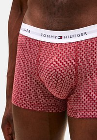 Bóxers rojos con un patrón repetido de logos blancos, con una pretina blanca que lleva la etiqueta "TOMMY HILFIGER". Tela suave y elástica.