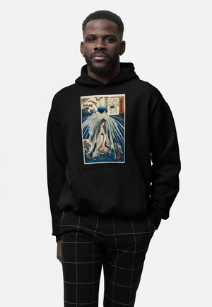 Sort hoodie med et grafisk print af en kvinde og bølger, i blå, hvid og rød detaljer. Kombinationen med ternede sorte bukser.