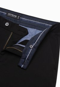 Schwarze Hose mit einem blauen Innenbund. Sie verfügt über einen Reißverschluss, einen Knopfverschluss und einen strukturierten Stoff. Das Etikett trägt die Aufschrift "Ombre Quintessence."
