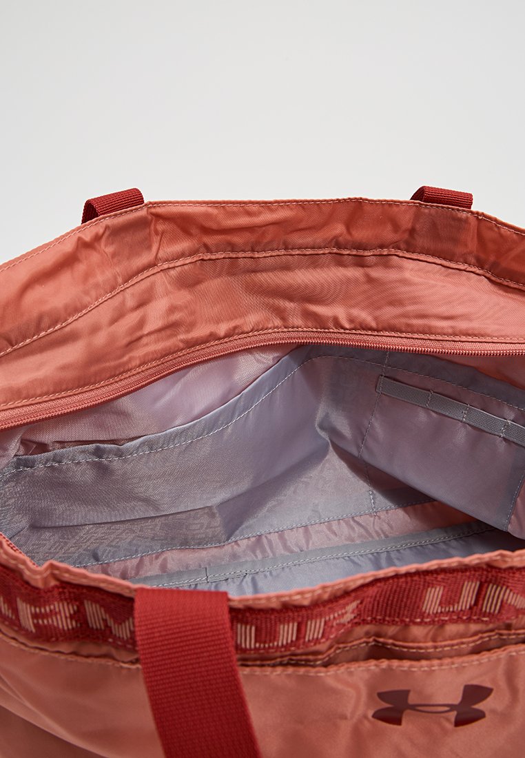 Interior de una bolsa tote de nylon roja, con un forro suave en gris claro, un bolsillo con cremallera y compartimentos abiertos. Se pueden ver asas resistentes en la parte superior.