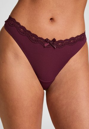 Kastanjebruine geribbelde bikini-onderbroek met kanten randje en een klein satijnen strikje op de taille en de bovenbenen van een persoon.