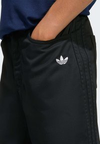Black athletic shorts made of smooth fabric, featuring a white Adidas logo on the left thigh and side pockets with vertical stripes.