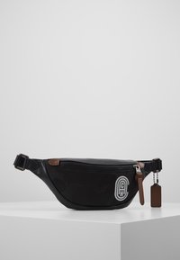 Černý ledvinka s texturovaným povrchem, přední kapsou na zip a koženým akcentem. Obsahuje logo a štítek na klíče.