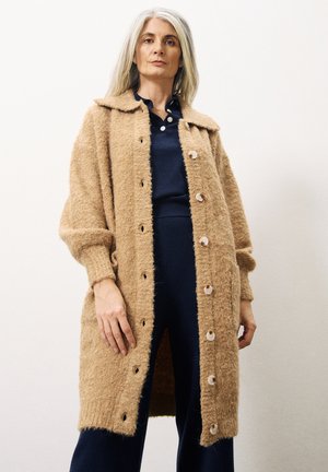 Beige, pluizige wollen cardigan met een knoopsluiting, puntige kraag en zijzakken. Lange, losse mouwen met ribgebreide manchetten.