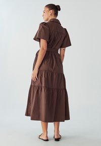 Rjava bombažna maksi obleka s kratkimi nabranimi rokavi, z pasom in plastenimi volani na robu. Gladka tekstura, podrobnost s ovratnikom.