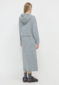 Abito grigio in maglia con cappuccio, caratterizzato da un top corto e una gonna lunga. Texture morbida, polsi a costine e spacchi sull'orlo per una maggiore libertà di movimento.