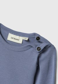 Maglietta a maniche lunghe azzurro chiaro con scollo rotondo, caratterizzata da due bottoni a pressione neri sulla spalla e una morbida texture in cotone.