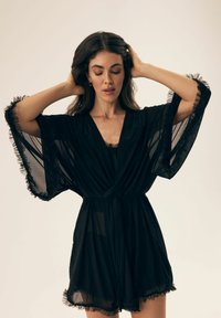 Czarna, półprzezroczysta szlafrok-kimono z szerokimi rękawami i falbanami. Związany w talii, warstwowy krój, lekko przezroczysty materiał.
