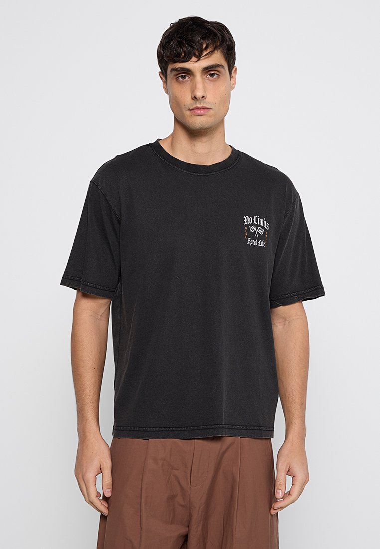 T-shirt en coton noir à col rond, à manches courtes, avec un imprimé graphique "No Limits" sur la poitrine. Coupe décontractée.