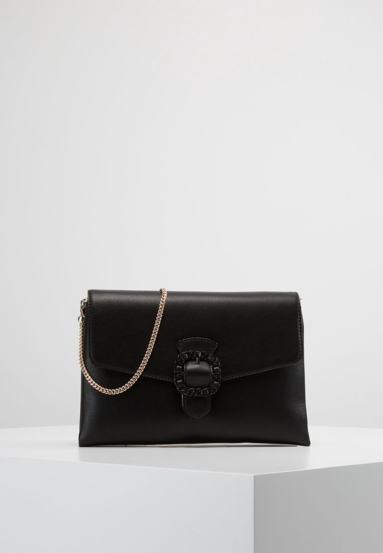 Sac à main en cuir noir avec une finition texturée, une bandoulière en chaîne dorée et un fermoir décoratif proéminent au design en maillons de chaîne.