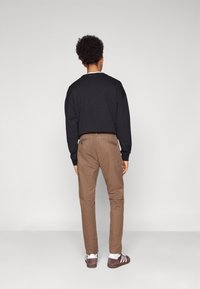 Svart sweatshirt med rund hals; bruna chinos med sidofickor; bruna skor med vita detaljer; enfärgad bakgrund.