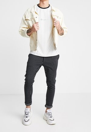 Camiseta blanca de rayas finas debajo de una chaqueta de denim clara, combinada con pantalones negros de rayas finas y zapatillas blancas.