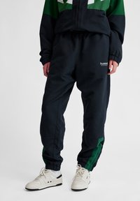 Námornícke jogger nohavice so zelenými bočnými doplnkami, elastický pás a úzky strih. V kombinácii s bielymi teniskami s čiernymi akcentmi.