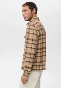 Camisa a cuadros marrón y beige en tela suave y texturizada; presenta cuello con solapa, puños con botones y un bolsillo en el pecho.