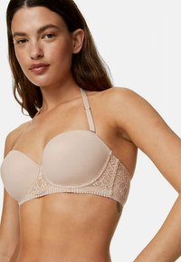 Beżowy bezramiączkowy biustonosz z gładkimi miseczkami, koronkowymi detalami po bokach i regulowanymi ramiączkami. Wykonany z miękkiego materiału z subtelnymi falbankami wzdłuż krawędzi.