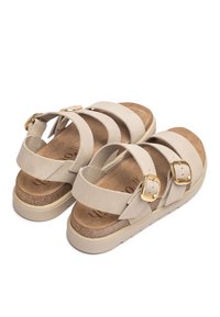 Beige suede sandals with two adjustable straps, gold buckles, and a cork footbed. Features a lightweight, textured sole for traction.
