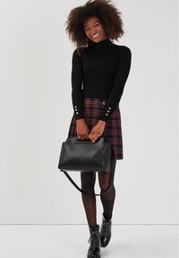 Sort ribbestrikket turtleneck, ternet nederdel med knapdetaljer, sort håndtaske og blanke snørebåndsstøvler til anklerne. Glatte teksturer og kontrasterende farver.