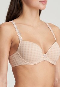 Beige ruudullinen rintaliivi, jossa on pehmustetut kupit, kukkakuvioinen pitsiolkainten reunassa ja koristeellinen keskityksessä. Pehmeä rakenne ja saumatonta muotoilua.