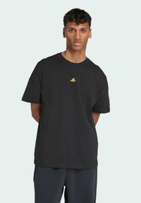 Sort bomulds T-shirt med korte ærmer og rund halsudskæring. Har et lille gult logo på brystet. Glat tekstur, afslappet pasform.