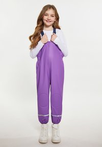 Violet vandens nepralaidūs kombinezonai su lygiu paviršiumi, elastinėmis apykaklėmis, atspindinčiais akcentais ir reguliuojamomis petnešomis, dėvimi ant balto marškinėlio.