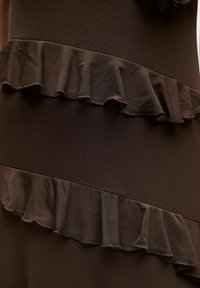 Tissu marron présentant des volants superposés. La texture est douce avec une subtile brillance. Les volants sont froncés et ont un bord ondulé.