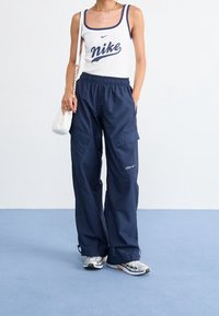 Biały top na ramiączkach z granatowymi wykończeniami i napisem „Nike”; granatowe spodnie cargo z elastycznym pasem i bocznymi kieszeniami; zestawione z srebrnymi sneakersami.