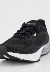 Scarpa sportiva nera con tomaia in rete, accenti riflettenti e suola bianca con motivi testurizzati. I lacci sono scuri con strisce intrecciate.