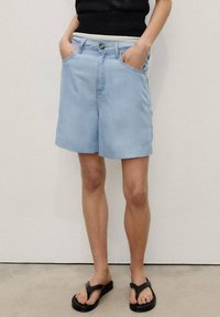Shorts en jean bleu clair avec une coupe décontractée, présentant une fermeture à bouton et à glissière, des passants de ceinture et des poches latérales. Texture de tissu lisse.