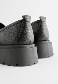 Čierne kožené slip-on topánky s textúrovaným povrchom a hrubou, odolnou čiernou podrážkou. Obsahujú jemné švy a zaoblený opätok.