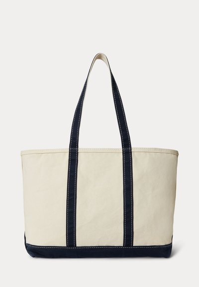 Geantă de pânză bej cu mânere și bază albastru închis, cu cusături albe de-a lungul bretelelor și marginilor, pe un fundal simplu.