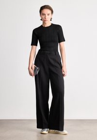 Juodas raukšlėtas trumpomis rankovėmis marškinėliai derinami su aukšto juosmens plačiomis kelnėmis. Aiški rankinė rankoje, o avalynė su sidabriniais akcentais.