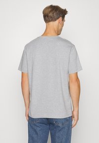 Siva kratka majica s kratkimi rokavi in okrolim izrezom, izdelana iz mehke bombažne tkanine, s sproščenim krojem in brez vidnih logotipov ali vzorcev.