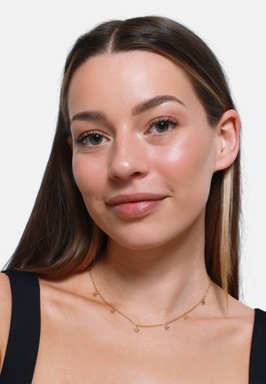 Gouden ketting met kleine stervormige accenten, verfijnd ontwerp, gedragen over een zwarte top, waardoor de sleutelbeenderen worden benadrukt.
