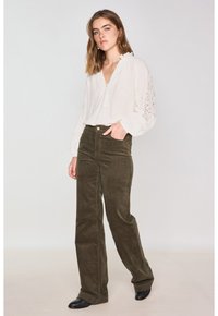 Blusa crema con dettagli in pizzo sulle maniche, abbinata a pantaloni in velluto a coste verde oliva. La modella indossa stivaletti neri.