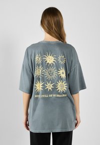 Oversized gray cotton T-shirt featuring yellow sun motifs and the text "SOUL FULL OF SUNSHINE" on the back. Short sleeves, relaxed fit.