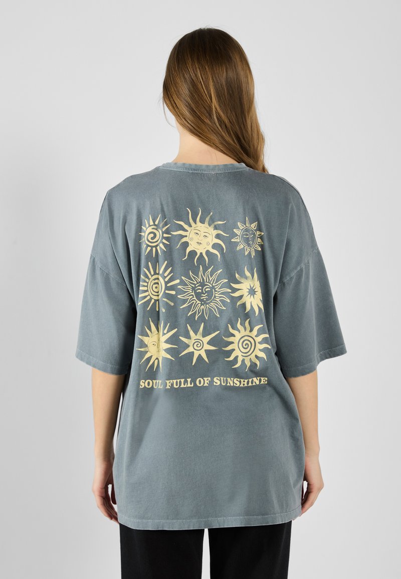 Oversized gray cotton T-shirt featuring yellow sun motifs and the text "SOUL FULL OF SUNSHINE" on the back. Short sleeves, relaxed fit.