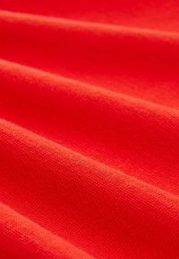 Rode stof met zichtbare textuur, met gladde, iets verhoogde lijnen in een doorlopende stroom. De kleur is egaal en levendig.