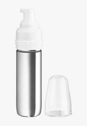 Flacon distributeur métallique avec pompe en mousse blanche et bouchon en plastique transparent retiré, sur fond uni.