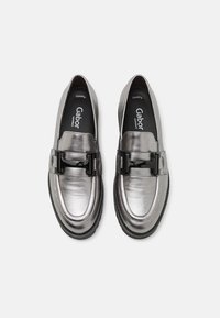Mocassins argentés métalliques avec une boucle noire en synthétique, présentant une texture lisse, un bout rond et une semelle en caoutchouc légère.