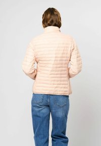 Ljust rosa, vadderad pufferjacka med hög krage, med synliga sömmar och en figurnära silhuett, kombinerad med blå denimjeans.